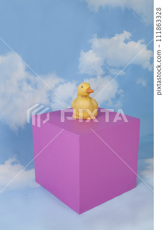 a plaster duck on a pink cube in front of a blue sky with clouds. a plaster duck on a pink cube in front of a blue sky with clouds. 111863328