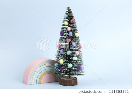 miniature christmas tree decorated with pompoms as baubles with a plastic rainbow toy next to him miniature christmas tree decorated with pompoms as baubles with a plastic rainbow toy next to him 111863331