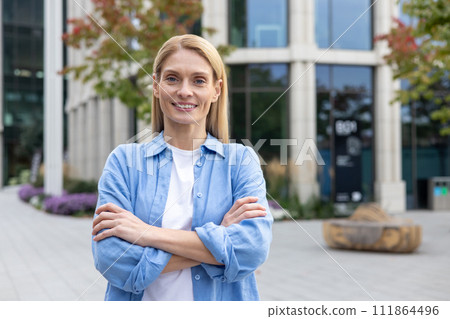A cheerful and confident businesswoman with crossed arms smiling outdoors, portraying professionalism and positivity. A cheerful and confident businesswoman with crossed arms smiling outdoors, portraying professionalism and positivity. 111864496