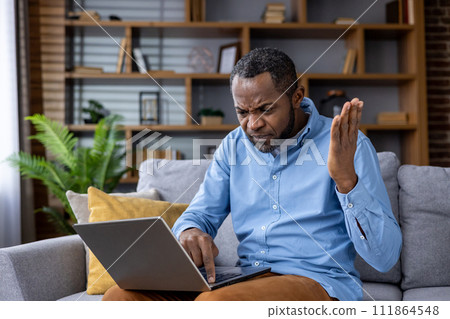 Confused African American man encounters computer problems, expressing frustration while working from home. Confused African American man encounters computer problems, expressing frustration while working from home. 111864548