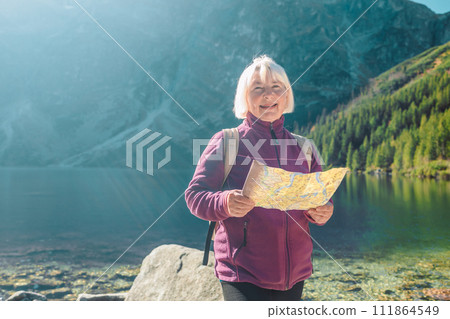 Shot of a senior 60s lost woman with smart phone holding a map while taking in the view from the top of a mountain. Female tourist in mountain read the map. Poland, Tatry Shot of a senior 60s lost woman with smart phone holding a map while taking in the view from the top of a mountain. Female tourist in mountain read the map. Poland, Tatry 111864549