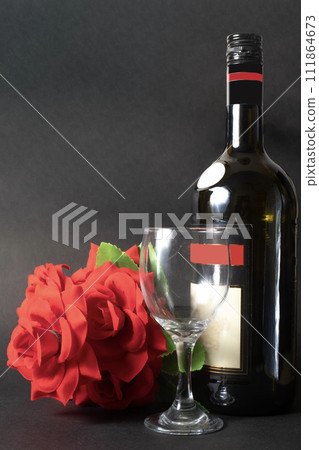 Wine bottle with a glass and a red rose on a black background. 111864673