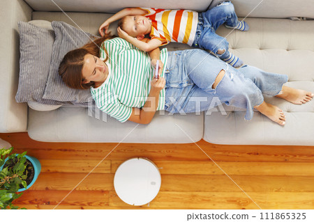 Mother and Child Relaxing on Couch with Smartphone and Robot Vacuum 111865325
