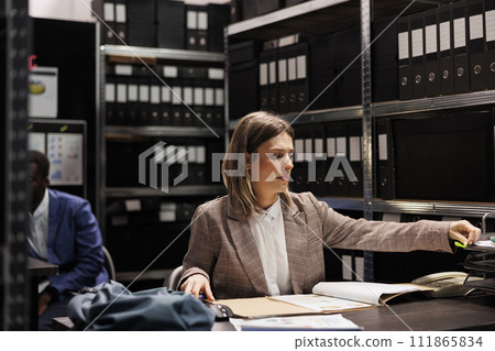 Investigator analyzing police report, checking crime case confidential information. Private detective in formal suit discovering mysterious victim files, working overtime in arhive room 111865834