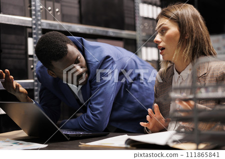 Investigators working at mysterious case, analyzing crime scene evidence in arhive room. Diverse private detectives discussing criminology department expertise, planning strategy to catch suspect Investigators working at mysterious case, analyzing crime scene evidence in arhive room. Diverse private detectives discussing criminology department expertise, planning strategy to catch suspect 111865841