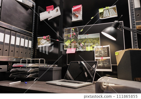 Empty dark police detective room with murder case investigation process on board. Suspect photographs connected with clues hanging on wall and file folders on racks in investigator agency office 111865855