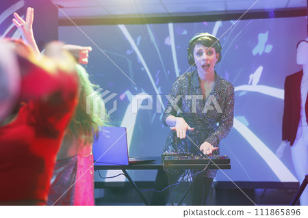 Excited woman dj mixing music using jog wheels on controller while performing on nightclub stage portrait. Young musician playing at discotheque party in club and looking at camera Excited woman dj mixing music using jog wheels on controller while performing on nightclub stage portrait. Young musician playing at discotheque party in club and looking at camera 111865896