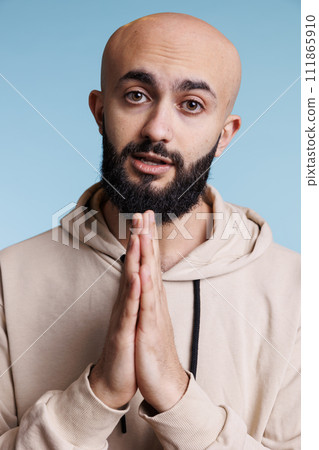 Young adult arab man with folded arms asking for help while looking at camera with pleading facial expression. Person pleasing, praying to god and making wish studio portrait Young adult arab man with folded arms asking for help while looking at camera with pleading facial expression. Person pleasing, praying to god and making wish studio portrait 111865910
