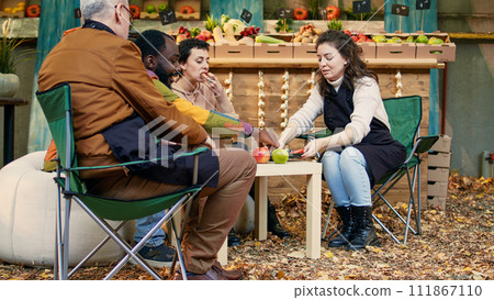 Clients having fun with business owners at food testing festival, trying out locally grown fruits and veggies. Cheerful customers and vendors eating bio produce and drinking homemade wine. 111867110