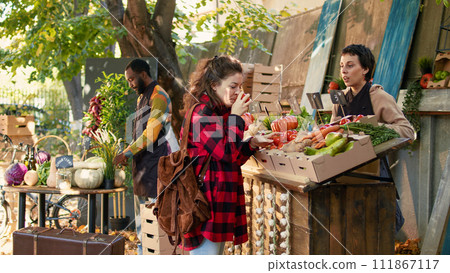 Small business owner selling fresh organic products from stand, talking to customer about healthy eating and local natural veggies. Female person asking market stall holder about bio products. 111867117
