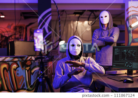 Anonymous hackers recording ransom scam on smartphone while doing illegal activities. Criminals streaming threat online and committing cyberattack in abandoned warehouse at night Anonymous hackers recording ransom scam on smartphone while doing illegal activities. Criminals streaming threat online and committing cyberattack in abandoned warehouse at night 111867124