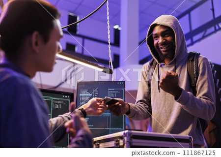 Smiling cheerful illegal malware developer holding ssd with computer virus. Happy hacker giving hard drive with malicious software to crime partner to steal information from database Smiling cheerful illegal malware developer holding ssd with computer virus. Happy hacker giving hard drive with malicious software to crime partner to steal information from database 111867125