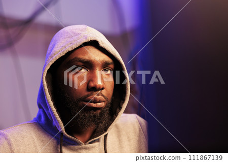 African american hacker breaching system security and stealing sensitive information. Young criminal in hood breaking law while cracking password and using spyware close up 111867139