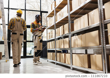 African american warehouse employee in headphones overseeing parcels security and maintenance. Post office shipment operator listening to music and working in storage room African american warehouse employee in headphones overseeing parcels security and maintenance. Post office shipment operator listening to music and working in storage room 111867210