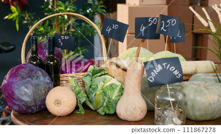 Variety of fresh locally grown lettuce and cabbage next to donations jar, colorful ripe natural products on farmers market stand. Organic produce on counter and table with coins. Close up. 111867278