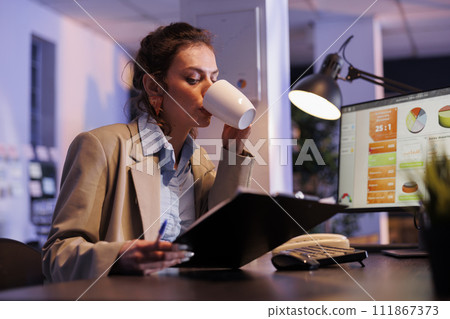 Executive manager checking marketing statistics drinking coffee, working late at night at financial strategy in startup office. Corporate employee planning investment plan to increase profit Executive manager checking marketing statistics drinking coffee, working late at night at financial strategy in startup office. Corporate employee planning investment plan to increase profit 111867373