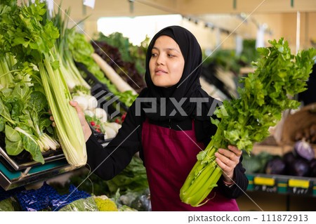 Muslim female seller in apron takes celery leaf from window Muslim female seller in apron takes celery leaf from window 111872913