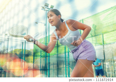 Young woman padel tennis player trains on the outdoor court Young woman padel tennis player trains on the outdoor court 111872914
