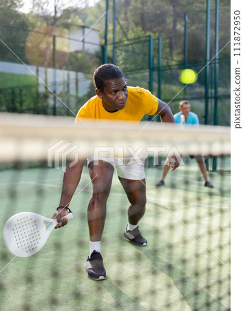 Male players playing padel in a padel court outdoor behind net 111872950