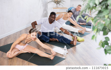 Young woman doing Janu Sirsasana during group yoga class Young woman doing Janu Sirsasana during group yoga class 111873015