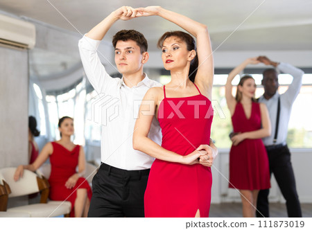 Positive woman and man dancing bachata in pair during group dance party Positive woman and man dancing bachata in pair during group dance party 111873019