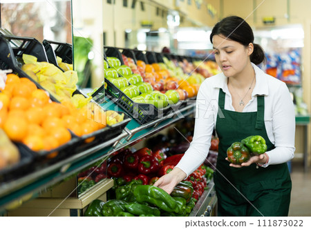 Young woman in uniform sells bell peppers in grocery store 111873022