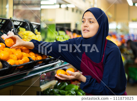 Muslim female seller in hijab chooses ripe mandarin Muslim female seller in hijab chooses ripe mandarin 111873025