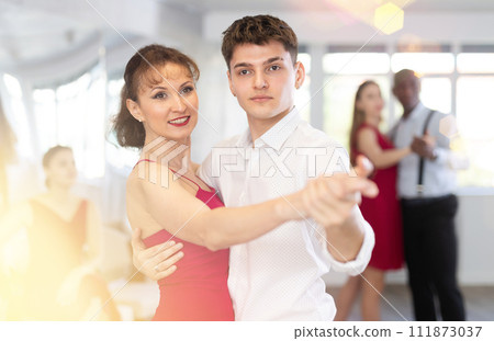 Young guy dancing waltz with female partner in red in dancing class Young guy dancing waltz with female partner in red in dancing class 111873037