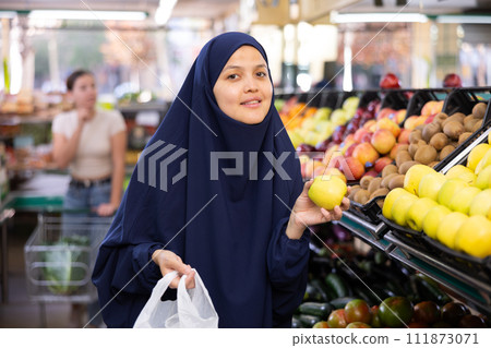 Young woman in hijab buys apples in grocery store 111873071