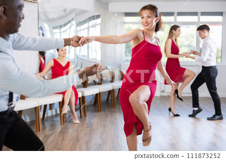 Cheerful woman in red practicing swing in pair during dance class 111873252