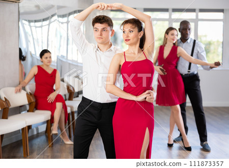 Hispanic guy practicing samba with woman in red in dance class 111873357