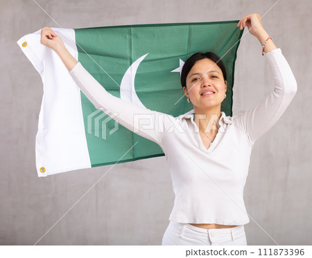 Reliant positive young woman holds big national flag of Pakistan with confident smile showing teeth Reliant positive young woman holds big national flag of Pakistan with confident smile showing teeth 111873396