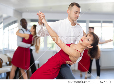 Smiling young woman in elegant red clothes learn to dance couples latin dance, energetic and fast tango in dance salon Smiling young woman in elegant red clothes learn to dance couples latin dance, energetic and fast tango in dance salon 111873405