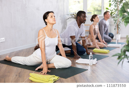 Young woman maintaining mental and physical health attending multinational group yoga class at studio, practicing twisting poses 111873550