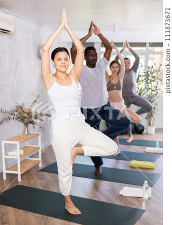 Happy woman in sportswear exercising with group active multinational people during yoga class in fitness center, standing in Happy woman in sportswear exercising with group active multinational people during yoga class in fitness center, standing in 111873671