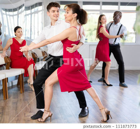 Hispanic guy and woman in red engrossed in passionate tango during dance class 111873773