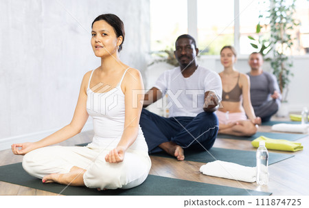Woman making yoga meditation in lotus pose for health care and wellness with group in fitness club Woman making yoga meditation in lotus pose for health care and wellness with group in fitness club 111874725