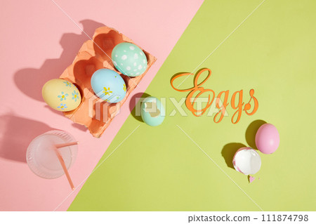Some lovely Easter eggs contained inside an egg carton painted in coral color. A glass cup filled with water containing two paintbrushes. The word Eggs made of paper featured Some lovely Easter eggs contained inside an egg carton painted in coral color. A glass cup filled with water containing two paintbrushes. The word Eggs made of paper featured 111874798