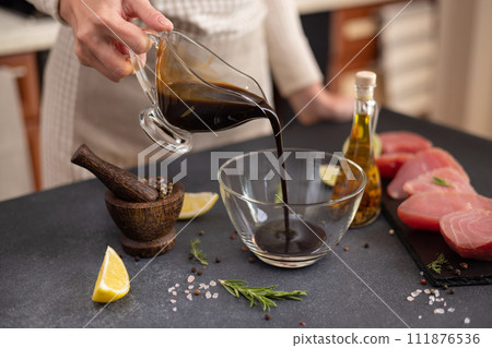 Woman pours soy sauce into glass bowl making marinade to marinate Pieces of Fresh tuna Fish fillet Woman pours soy sauce into glass bowl making marinade to marinate Pieces of Fresh tuna Fish fillet 111876536