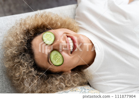 Young Woman Enjoying Skincare Routine with Cucumber on Eyes 111877904