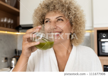 Smiling Woman Enjoying a Healthy Green Juice in Modern Kitchen Smiling Woman Enjoying a Healthy Green Juice in Modern Kitchen 111877906