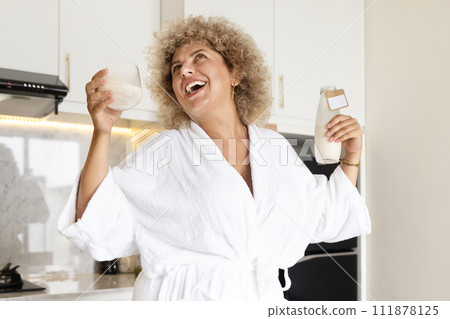 Joyful Woman in White Robe Enjoying Fresh Milk in Kitchen Joyful Woman in White Robe Enjoying Fresh Milk in Kitchen 111878125