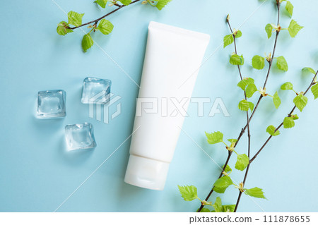 White Cream tube, young small leaves of birch tree, ice cubes on blue. Cosmetic skincare product blank plastic package. Bottle of moisturizer, sunscreen lotion, balsam, toothpaste mockup, flat lay. 111878655