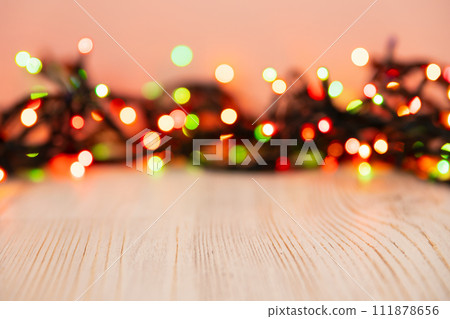 Blurred product background with Christmas New Year colorful light bulbs garland and wooden table. Selective focus, copy space for beauty product packaging, advertising backdrop. Empty place 111878656