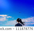 A girl watching a bird fly away in the blue sky. A composite image of the blue sky in the background and the AI-generated girl. 111878776