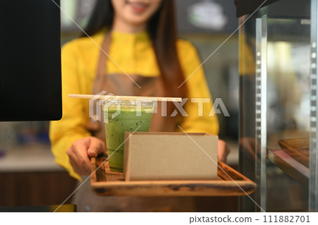 Female waiter in apron serving cold drink paper straw and cake in a cardboard takeaway box Female waiter in apron serving cold drink paper straw and cake in a cardboard takeaway box 111882701