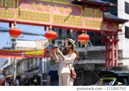 Happy young woman taking photo with vintage camera at Chinatown district in Thailand 111882742