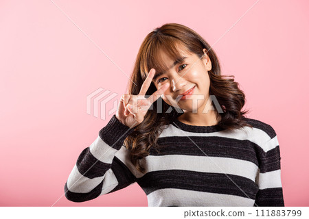 Asian happy portrait beautiful young woman smiling showing finger making v-sign victory gesture symbol near eye, studio shot isolated on pink background, female curly hair excited show two fingers Asian happy portrait beautiful young woman smiling showing finger making v-sign victory gesture symbol near eye, studio shot isolated on pink background, female curly hair excited show two fingers 111883799