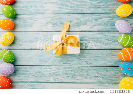 Happy Easter Day. Top view holiday banner background design with colorful easter eggs and gift box on blue wooden background with copy space, celebration greeting card Happy Easter Day. Top view holiday banner background design with colorful easter eggs and gift box on blue wooden background with copy space, celebration greeting card 111883808