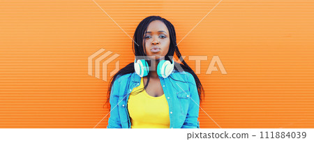 Portrait of young african woman listening to music in headphones on orange background Portrait of young african woman listening to music in headphones on orange background 111884039